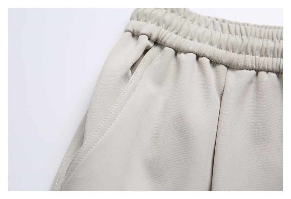 Close-up of light beige joggers showing the elastic waistband and curved front pocket stitching.