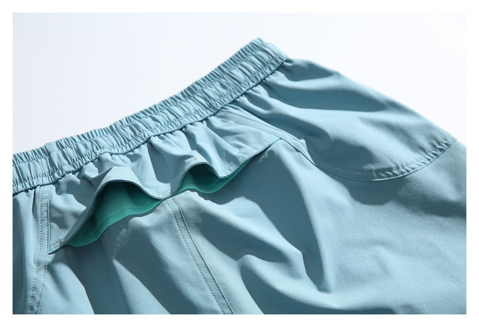 Close-up of light blue shorts with an elastic waistband, layered ruffle trim, and curved pocket stitching.