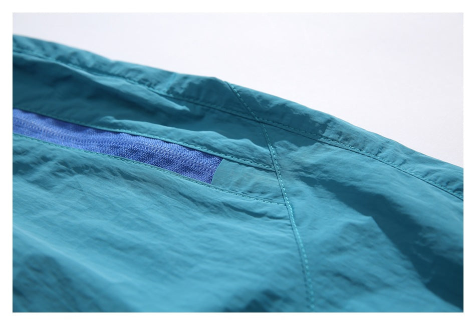 Close-up of teal shorts showing a blue zippered pocket and curved panel stitching.