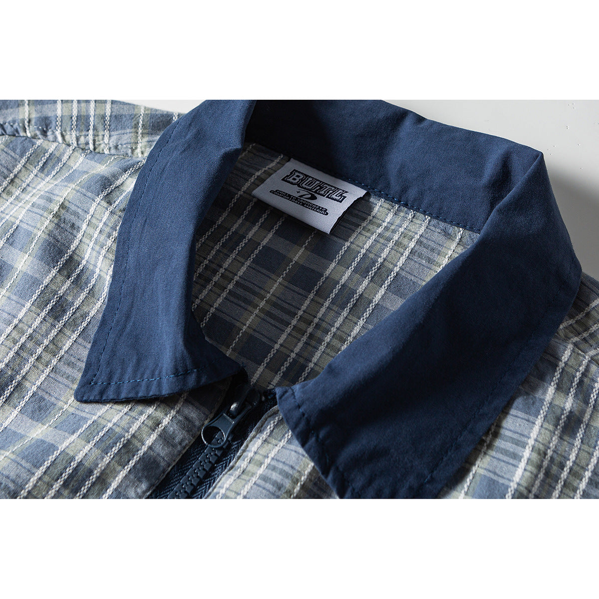 Close-up of a blue-gray plaid shirt with a navy collar, black zipper, and sewn-in neck label.