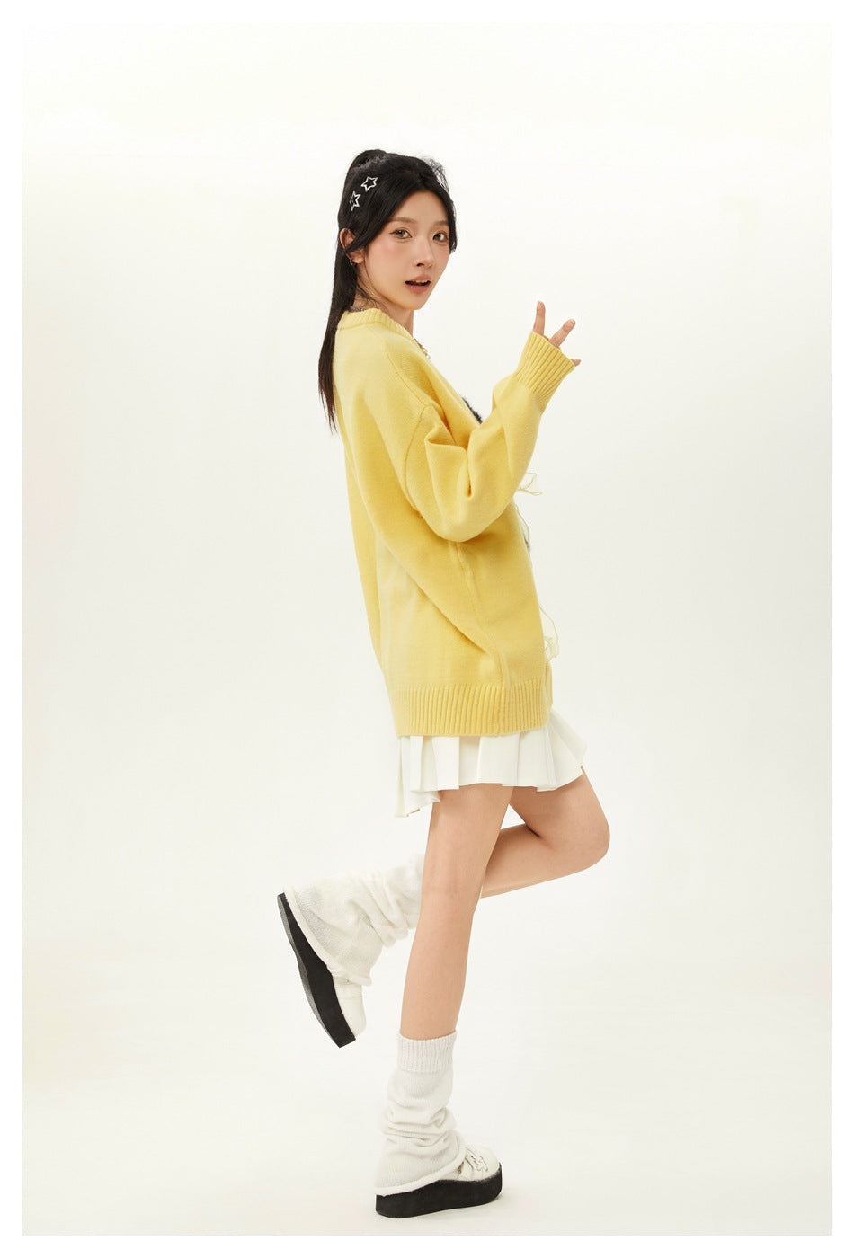 Side view of a model wearing a yellow oversized sweater and white pleated skirt.