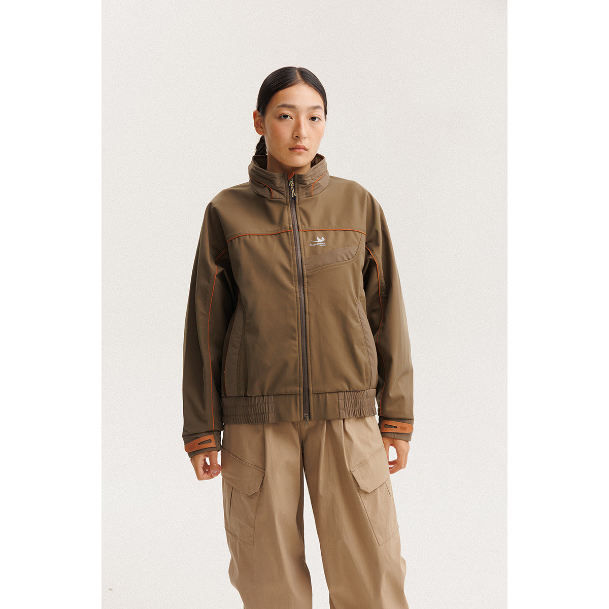 Model wearing a brown zip-front jacket with orange piping and tan cargo pants.