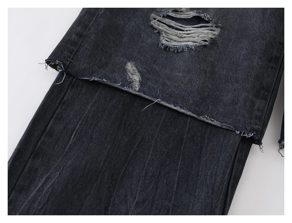Close-up of distressed dark jeans with frayed openings and a raw, unfinished edge.