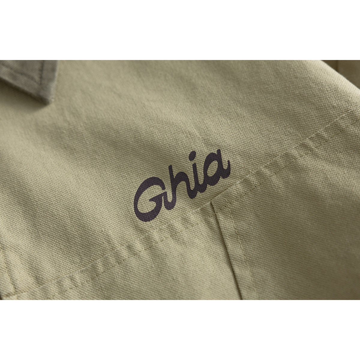 Close-up of a dark script logo printed on the chest of a khaki jacket.