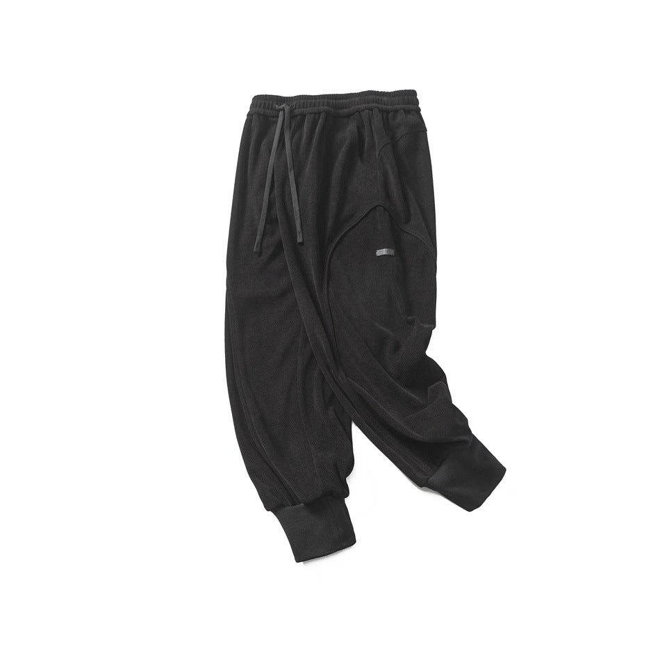 Full view of black pants laid flat, with a drawstring waist, curved seams, and wide ankle cuffs.