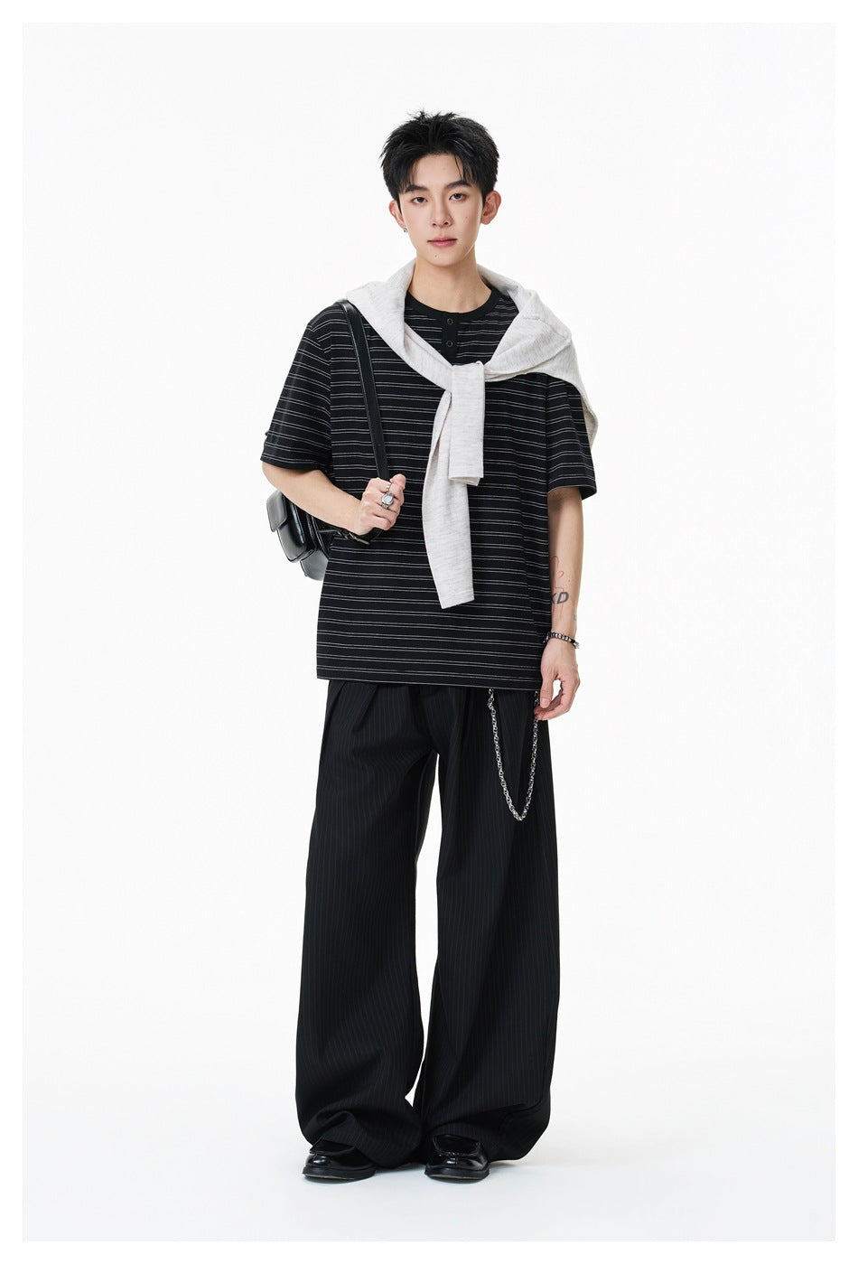 Model wearing a black striped two-button shirt with wide trousers and a light sweatshirt draped over his shoulders.