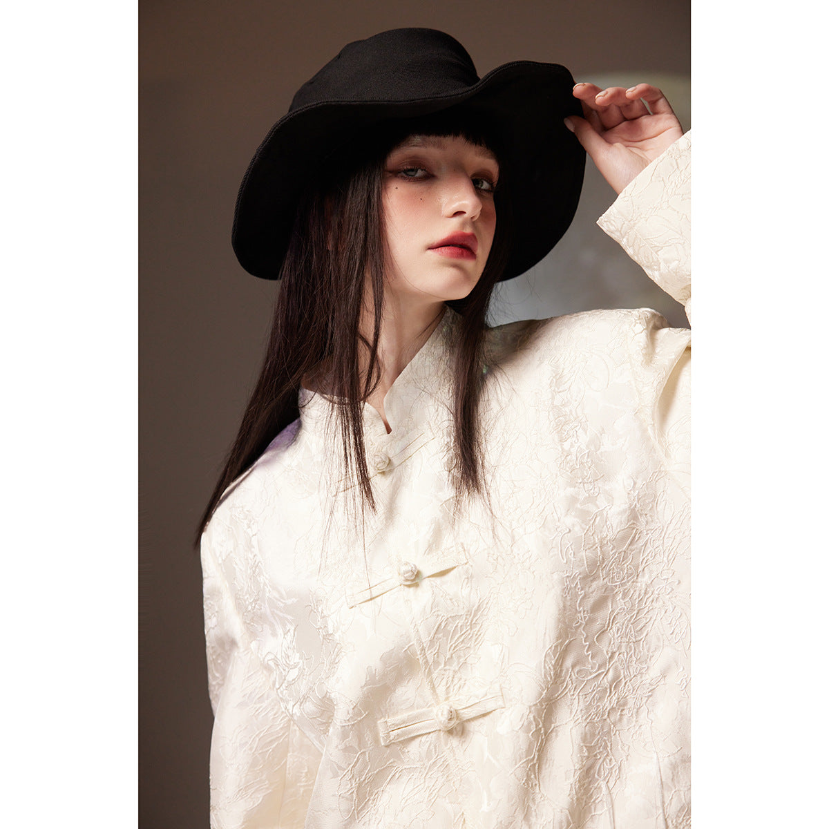 Close-up of a model in an ivory floral jacquard frog-button jacket and black wide-brim hat.
