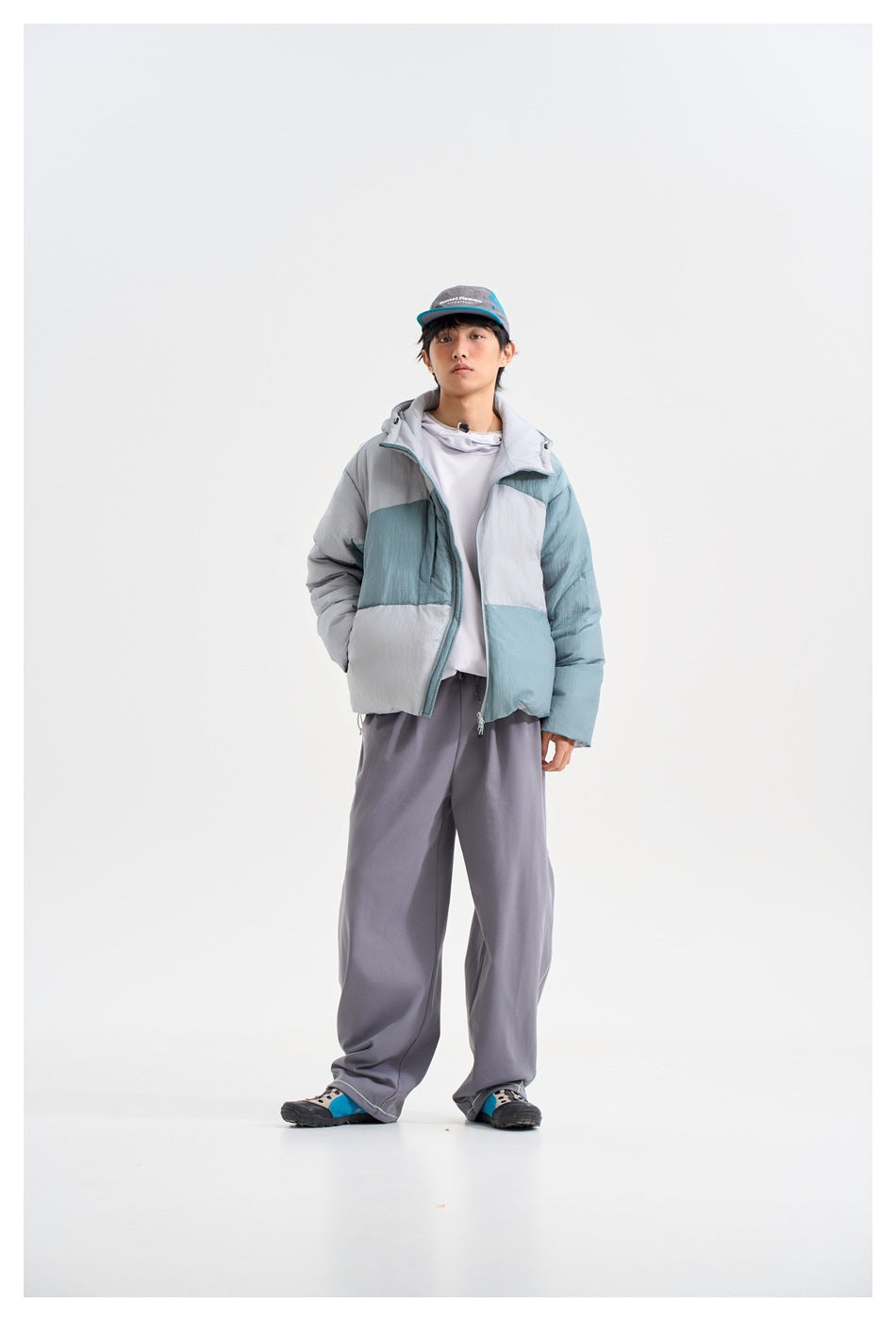 Front view of a model wearing a hooded puffer jacket with pale blue, gray, and white color-block panels.