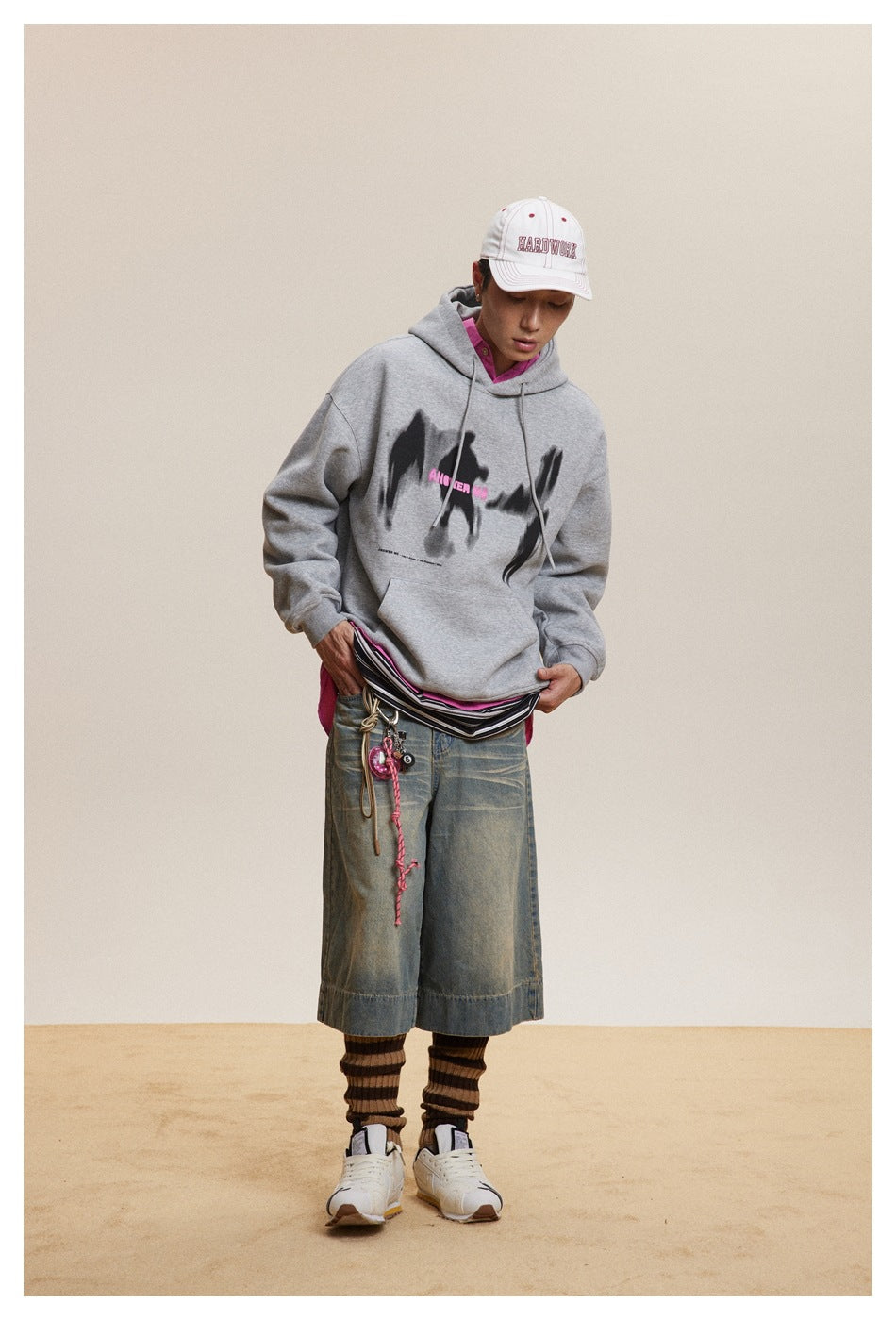 Model wearing a gray graphic hoodie and denim shorts, looking down while adjusting the layered waistband.