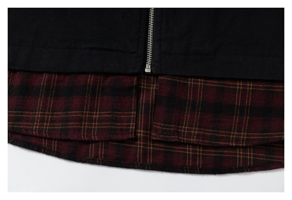 Close-up of a silver zipper above a burgundy and brown plaid hem on a black garment.