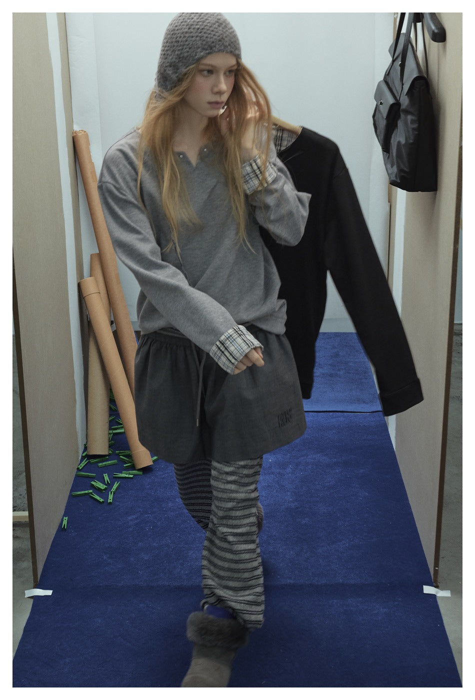 Model in gray V-notch top with plaid cuffs, holding a black matching top on a hanger in a styled setting