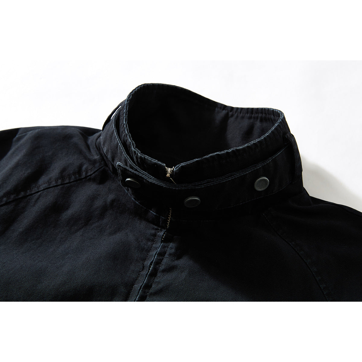 Close-up of a black jacket’s raised collar with a zipper and dark snap buttons.