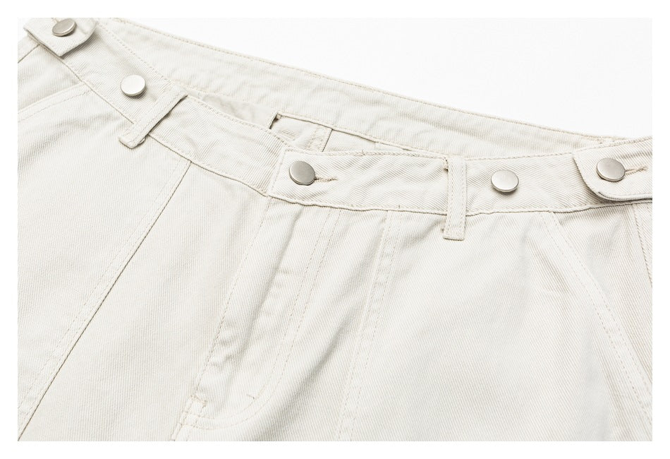 Close-up of off-white trousers showing the waistband, belt loops, metal buttons, and front fly.