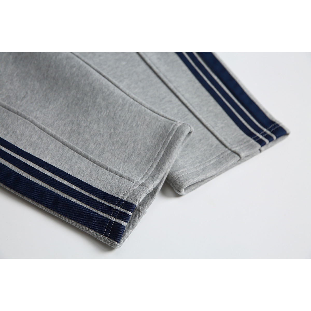 Close-up of gray jogger pant legs with navy-and-white striped hems and visible stitching.