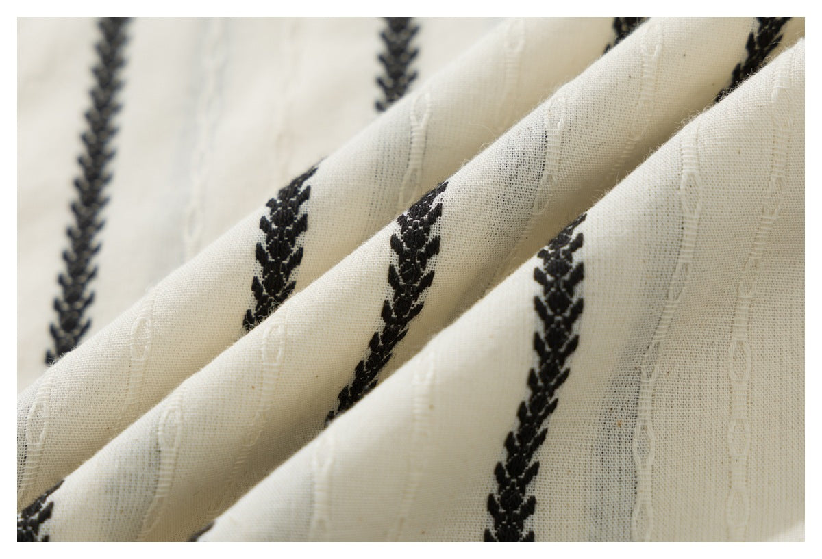 Close-up of ivory fabric with repeating black braided motifs and subtle white stitched stripes.