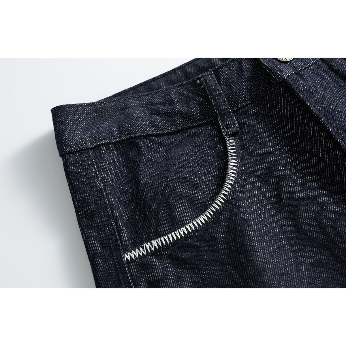 Close-up of a curved front pocket on dark indigo jeans, outlined with bold white stitching.