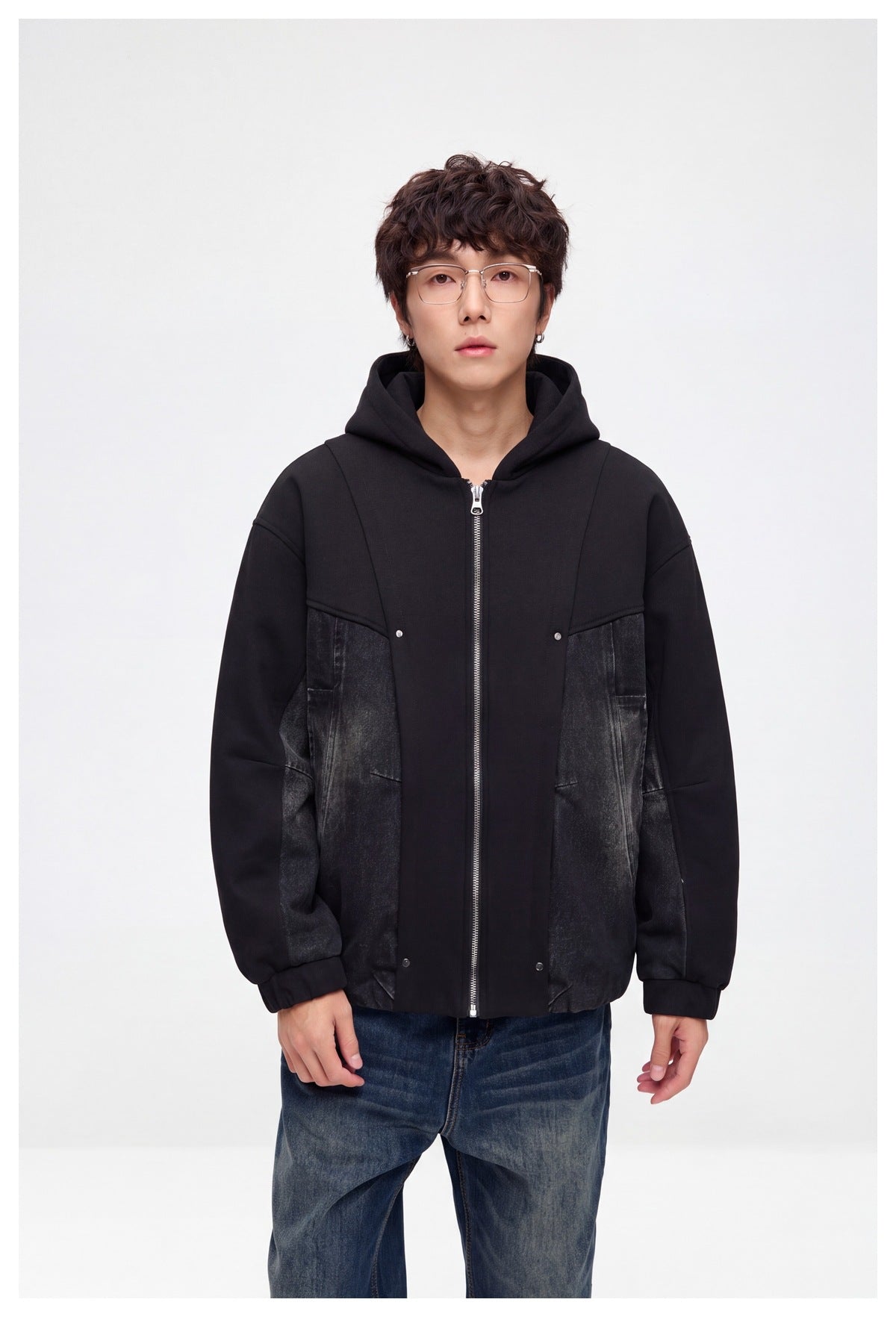 Man wearing a black hooded zip jacket with washed denim-look panels over blue jeans, front view