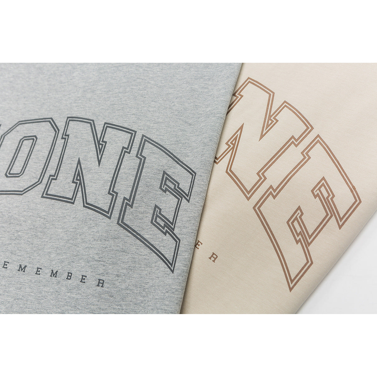 Close-up of outlined collegiate-style lettering printed on gray and cream T-shirts.