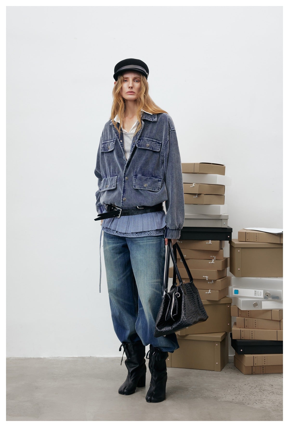 Model facing forward in the blue corduroy jacket with flap pockets, layered over a pleated top and jeans