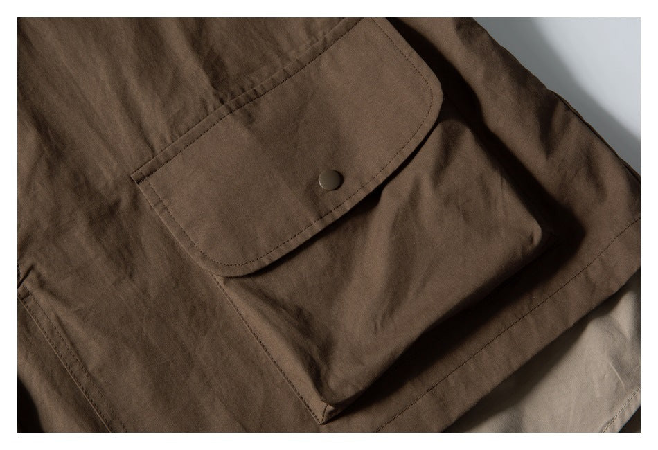 Close-up of a dark brown garment's large flap pocket with a single snap button.