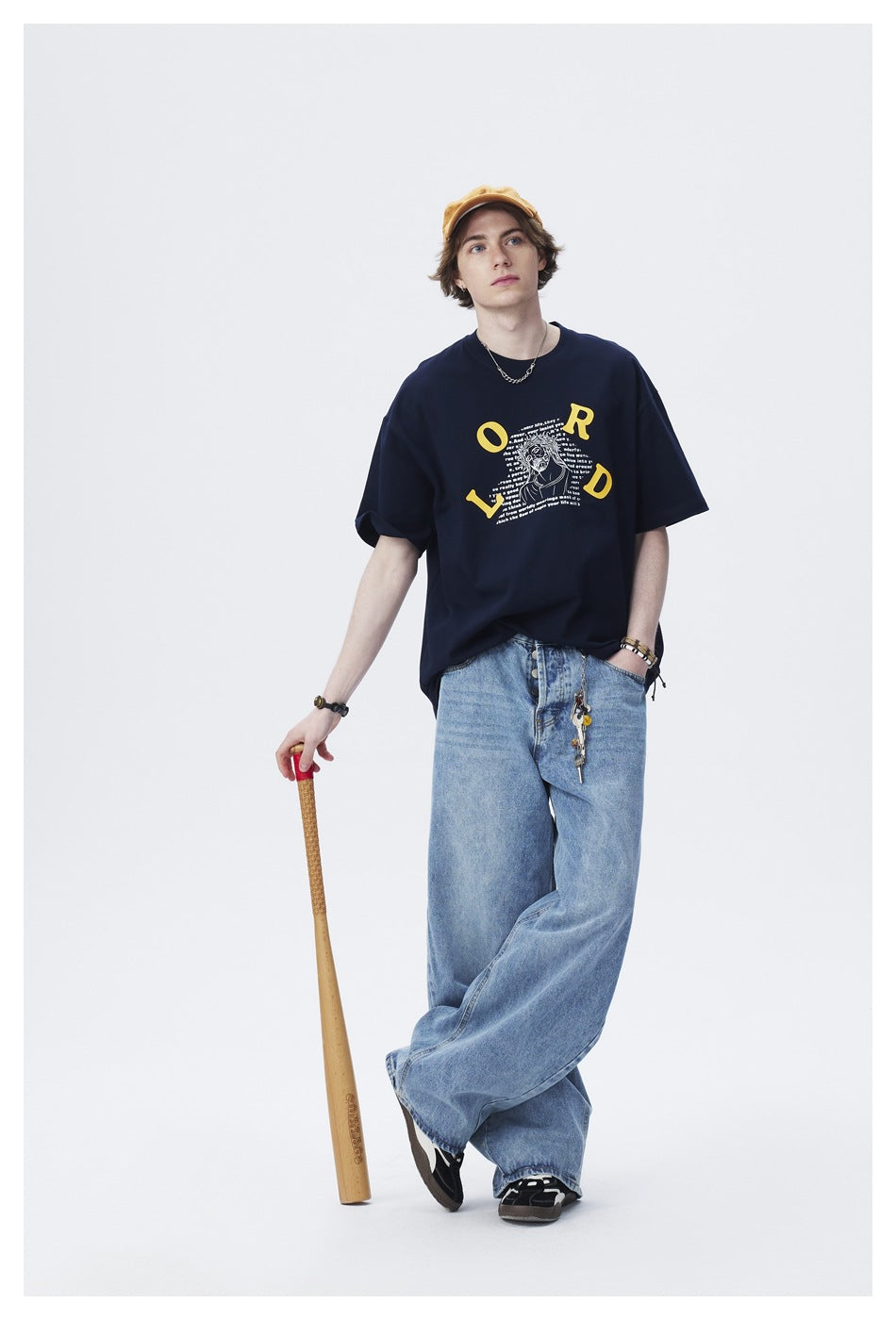 Model wears a navy graphic T-shirt and loose light-blue jeans with a mustard cap.