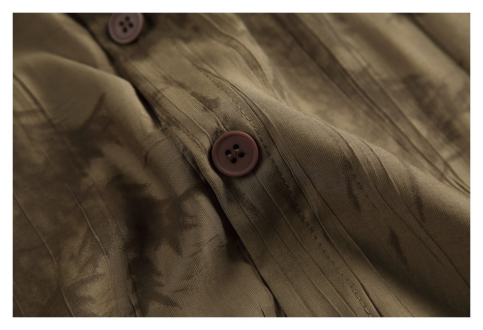 Close-up of a brown button and stitched placket on an abstract-patterned shirt.