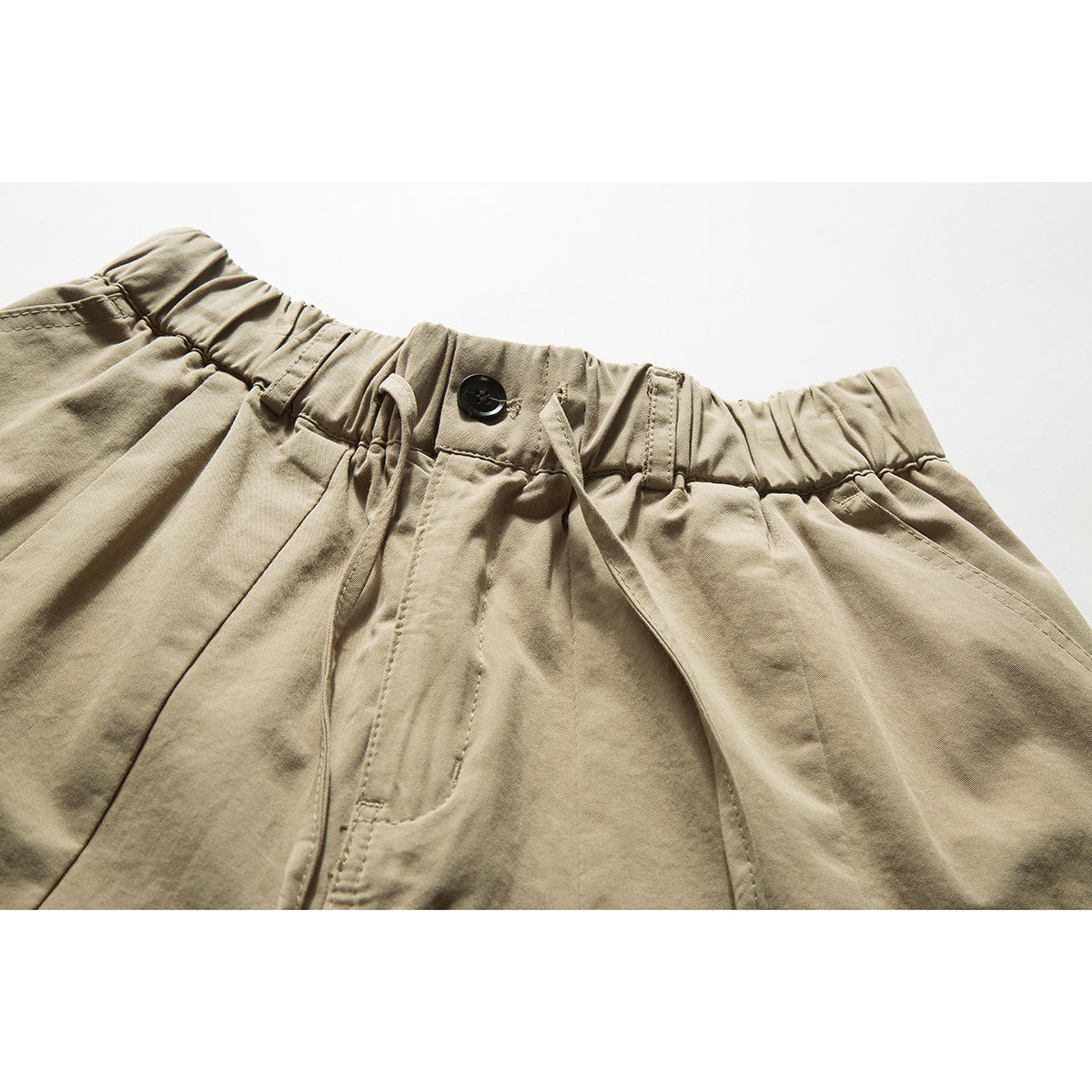 Close-up of khaki shorts showing an elastic waistband, button, drawcord, belt loops, and front pocket seams.