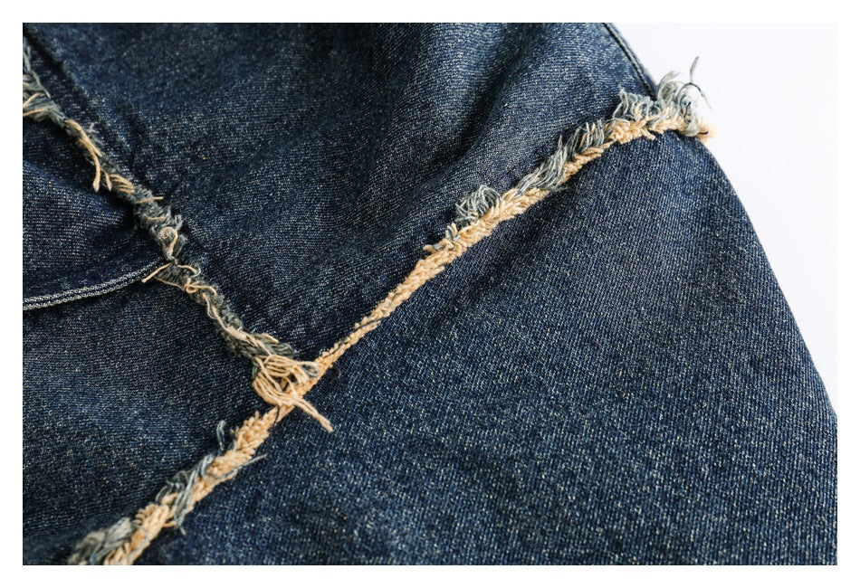 Close-up of dark denim jacket panels joined with exposed, frayed seams and tan threads.