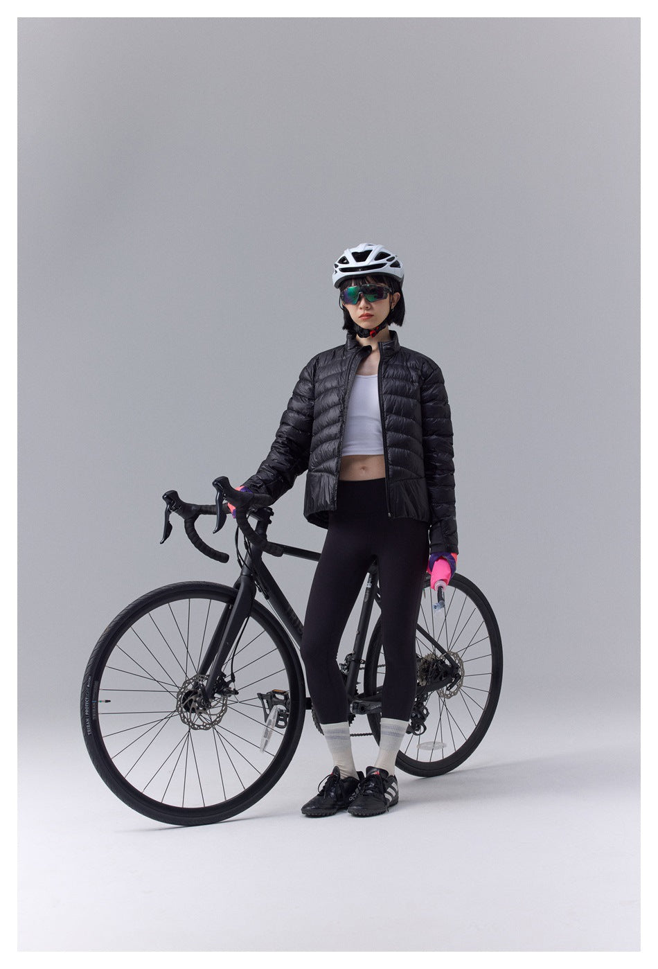 Model in black quilted zip jacket with white top and black leggings standing beside a road bike