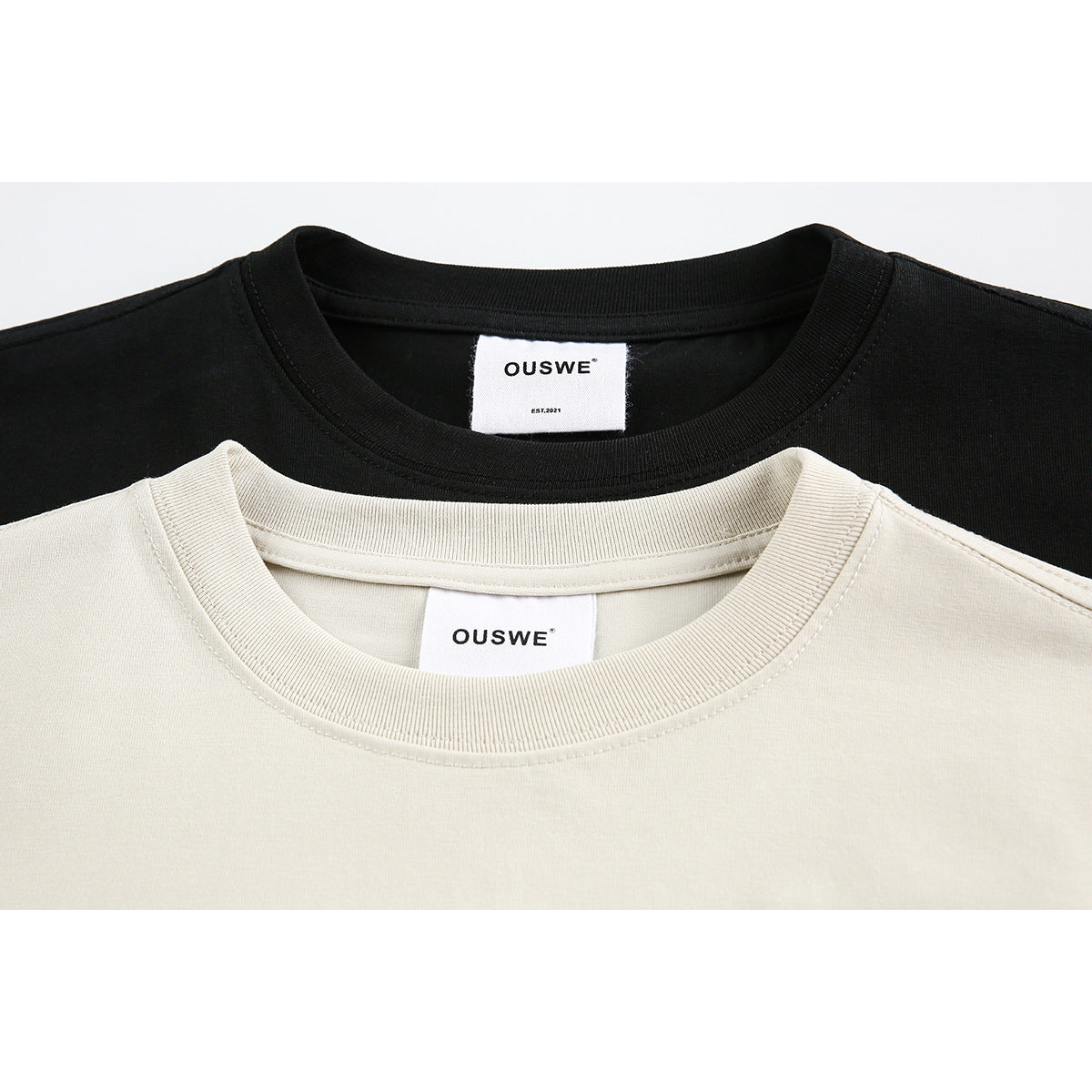 Close-up of cream and black T-shirt crew necks with visible OUSWE neck labels.