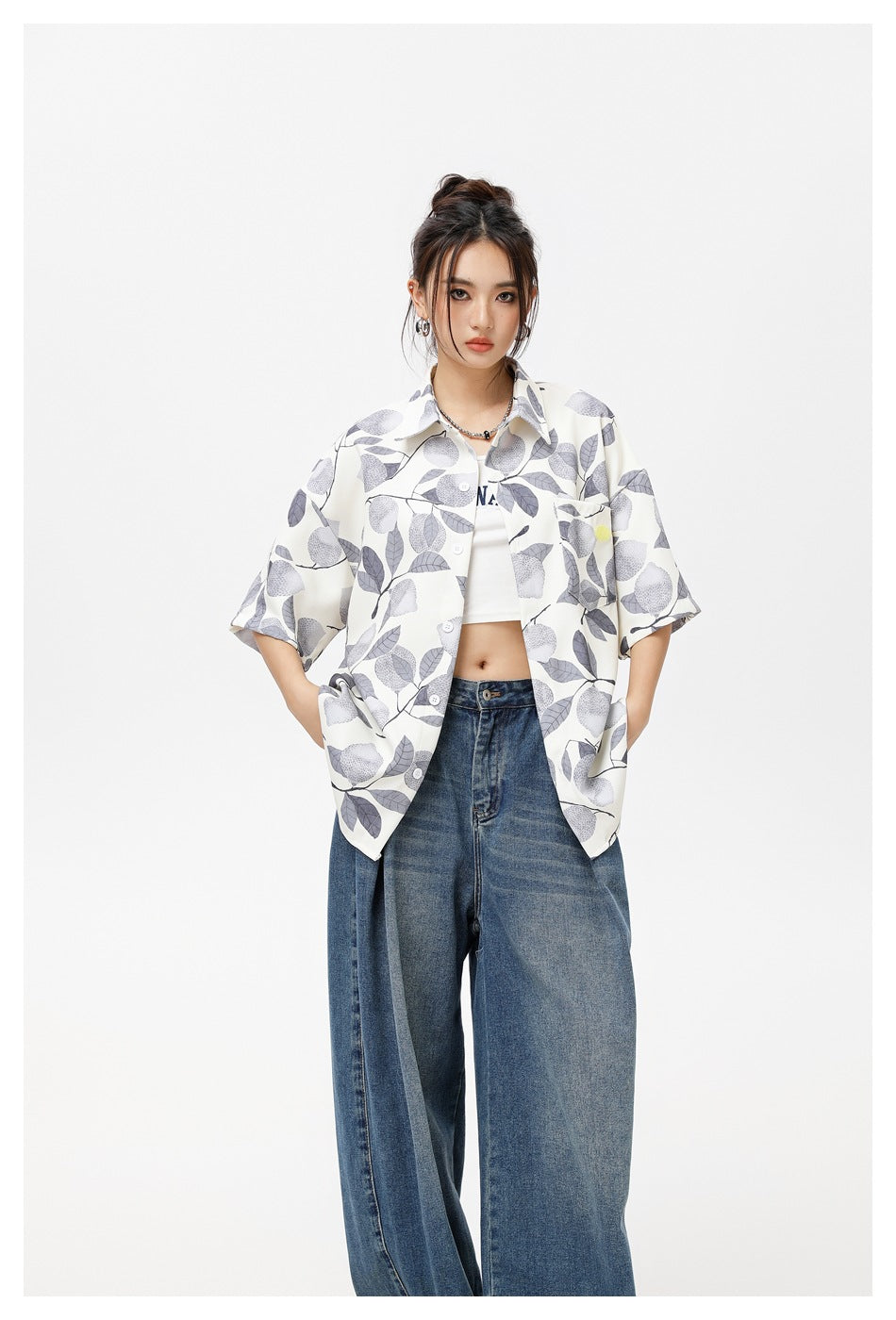Front view of a model wearing an oversized ivory button-up shirt with a gray botanical print and blue jeans.