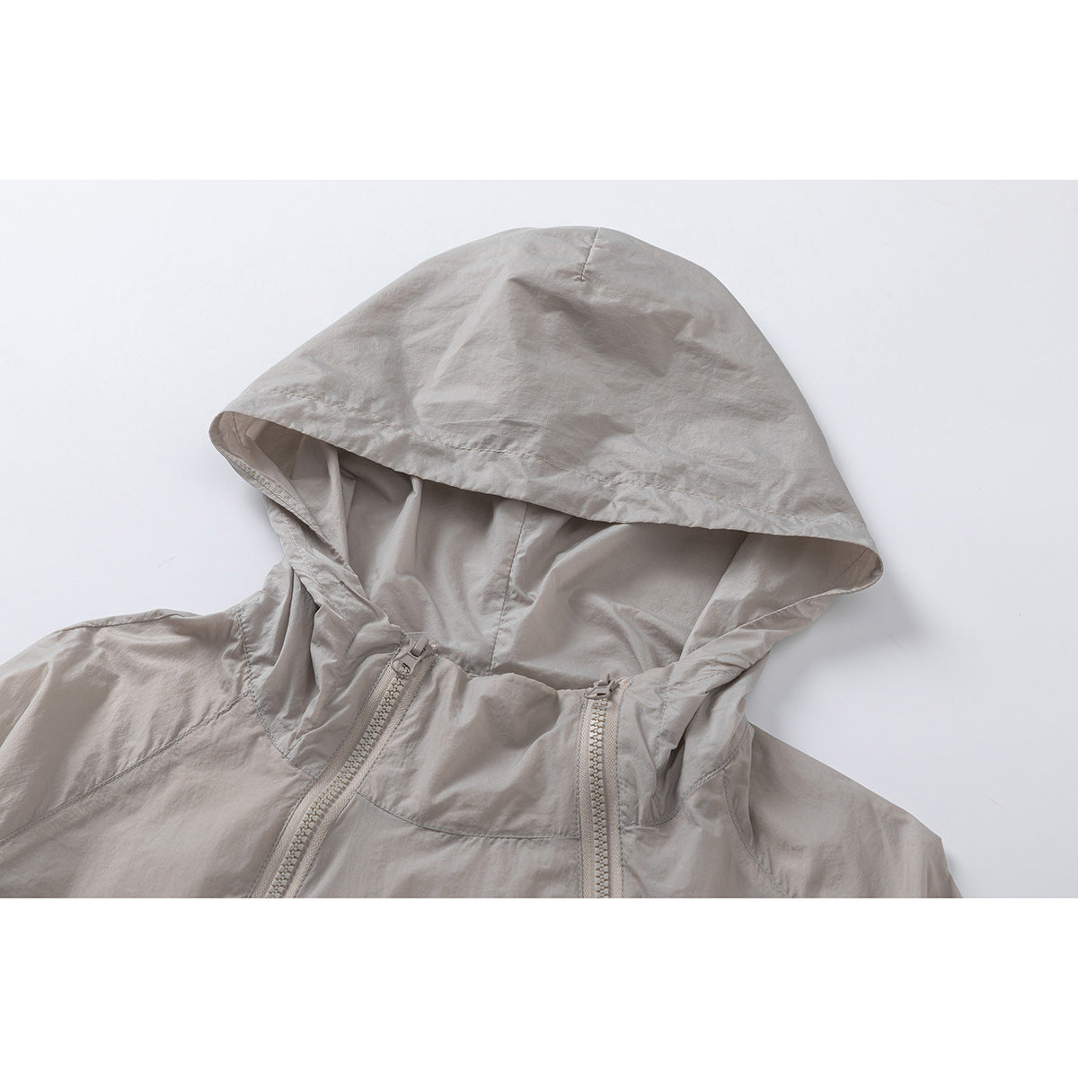Close-up of a light taupe jacket hood and upper chest, showing the hood opening and two front zippers.
