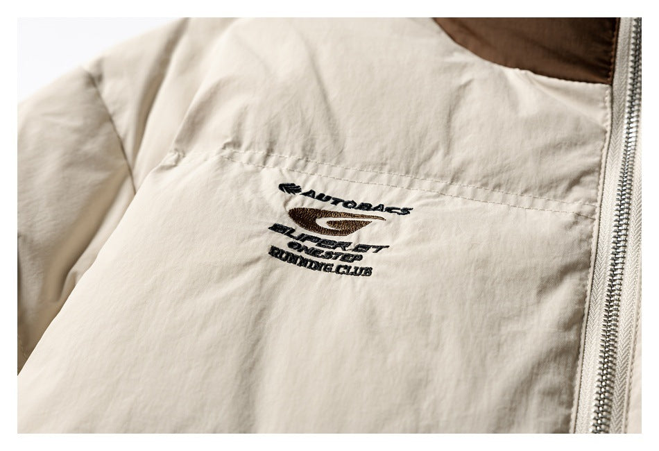 Close-up of a cream jacket panel with dark embroidered lettering and a silver zipper.