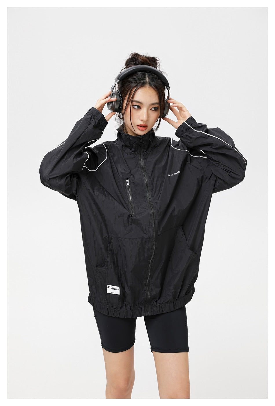 Front view of a model wearing a black oversized zip-up jacket with white piping and a high collar.