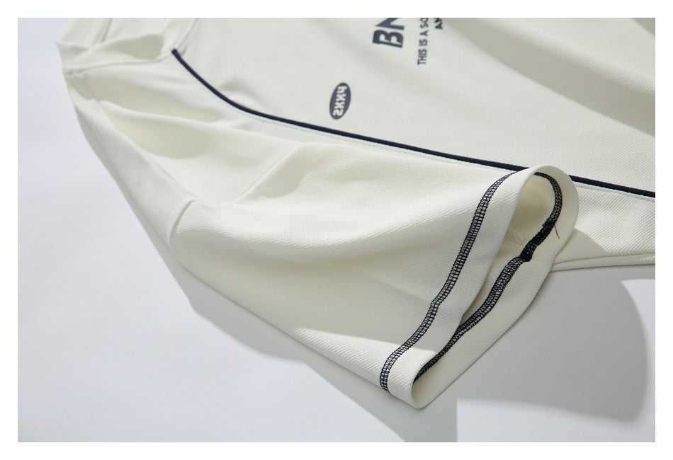 Close-up of an ivory shirt sleeve and body with navy piping, folded cuff, and partial dark print.