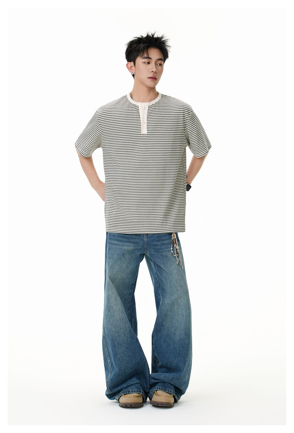 Model wearing a loose gray-and-white striped short-sleeve henley with blue wide-leg jeans, hands at his hips.