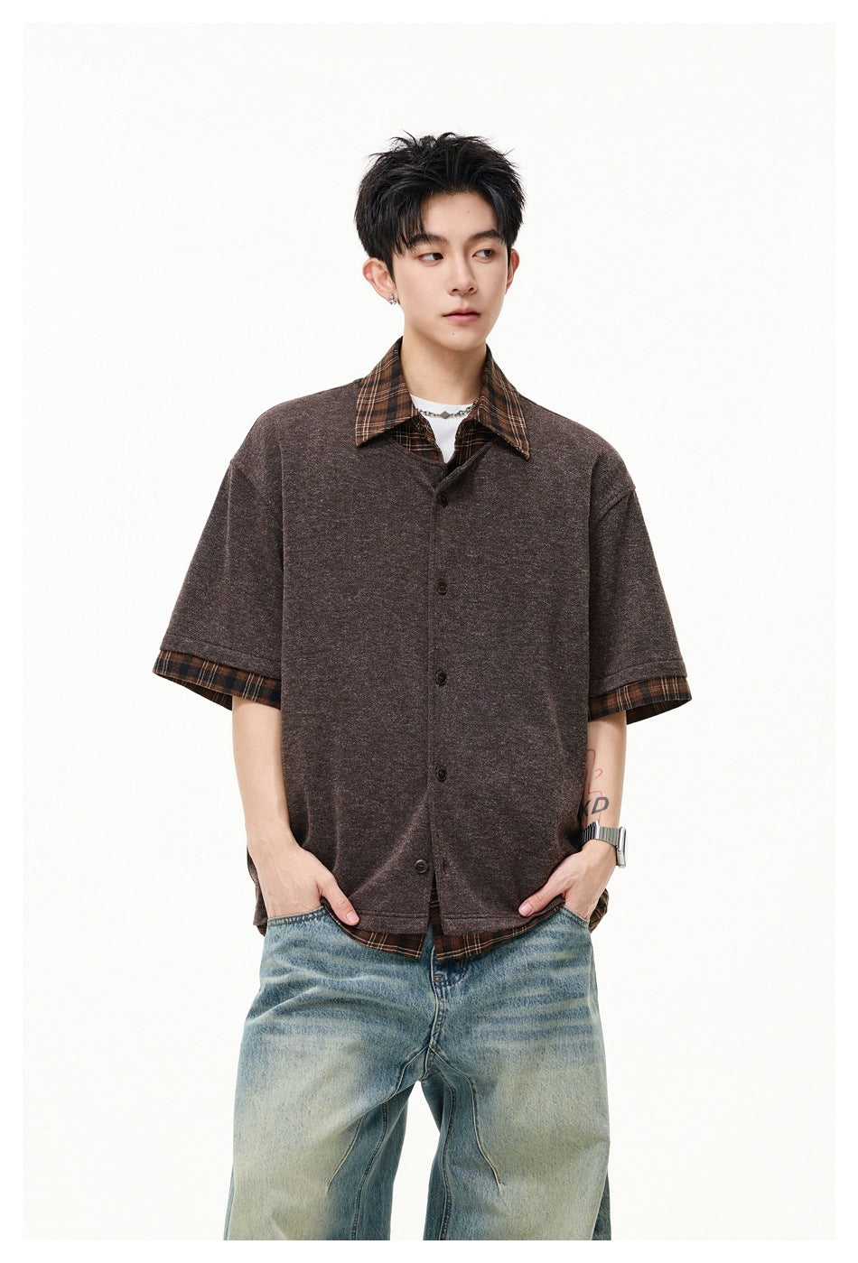 Model wearing a buttoned brown short-sleeve top with a plaid collar, cuffs, and hem over a plaid shirt.