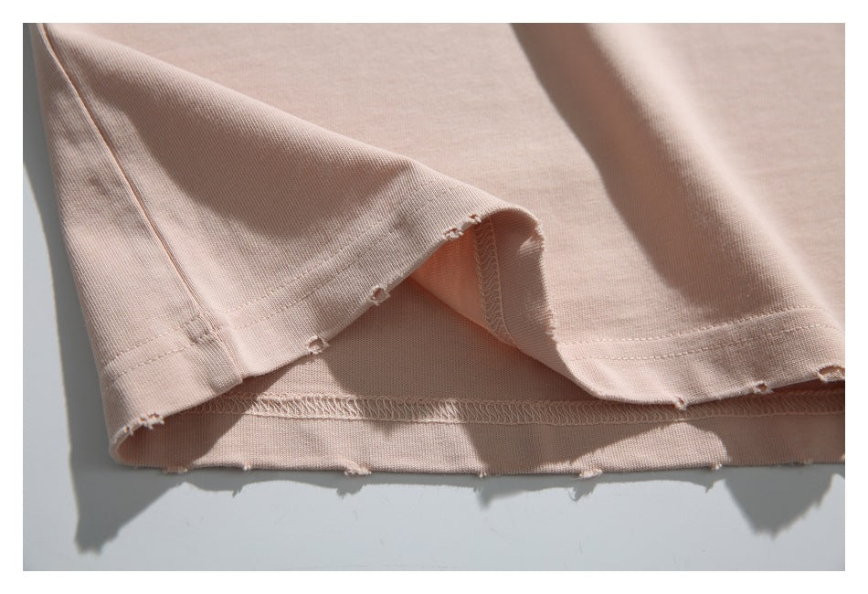 Close-up of the pale blush-pink T-shirt hem turned back to show the overlocked seam and frayed edge.