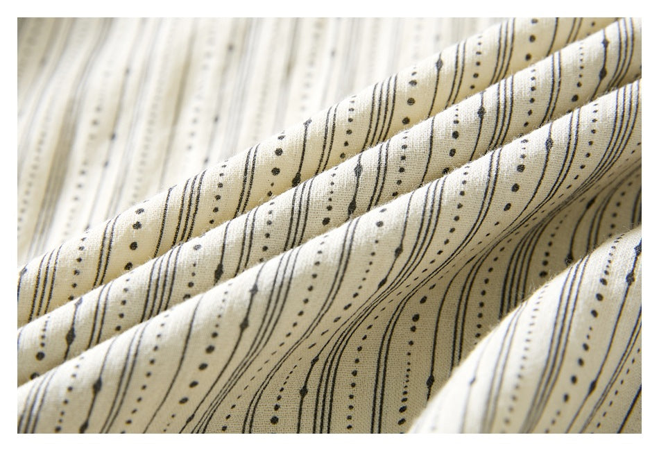 Close-up of ivory fabric gathered into folds, patterned with narrow black lines and dots.