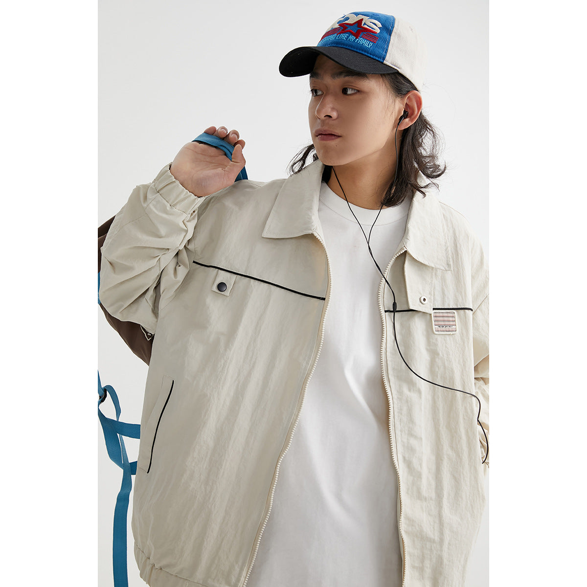Model wearing an open ivory zip jacket with black piping, chest patch and elastic cuffs.