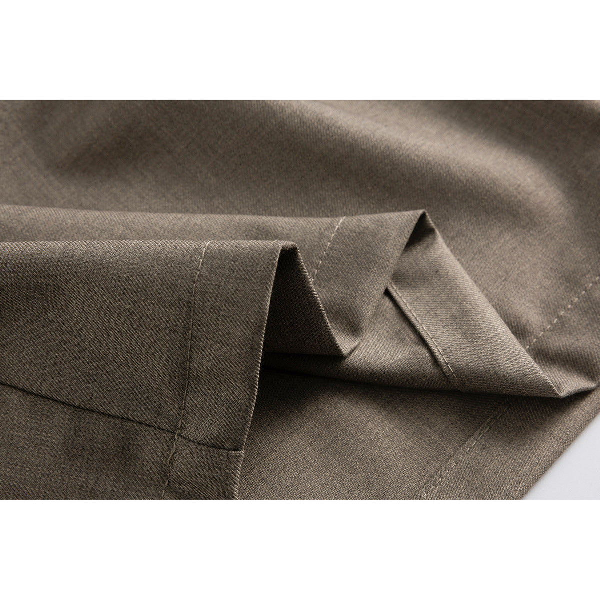 Close-up of taupe shorts showing folded leg fabric and hem stitching.