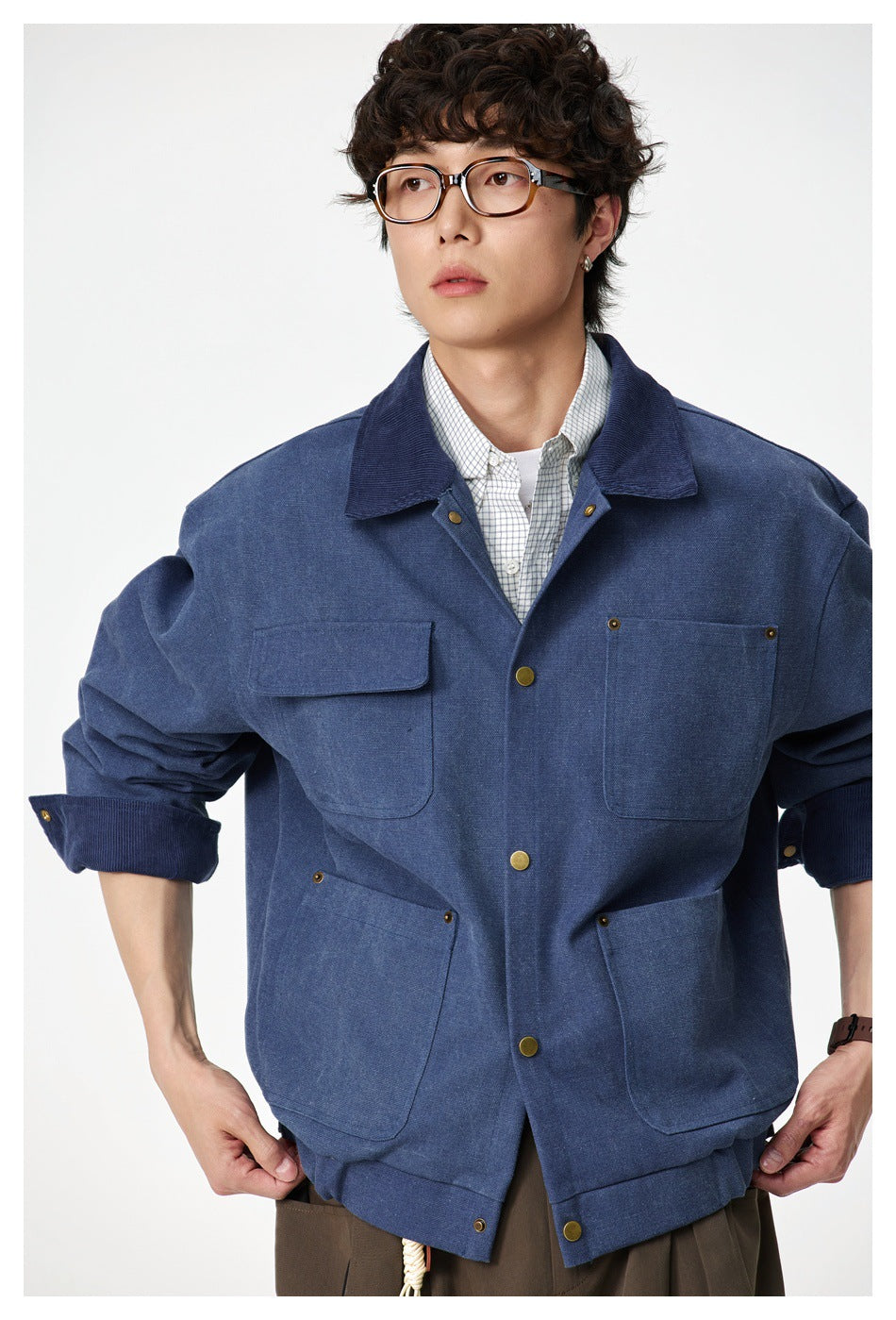 Close view of a model wearing a blue work jacket with four pockets, brass-tone buttons, and a dark collar.