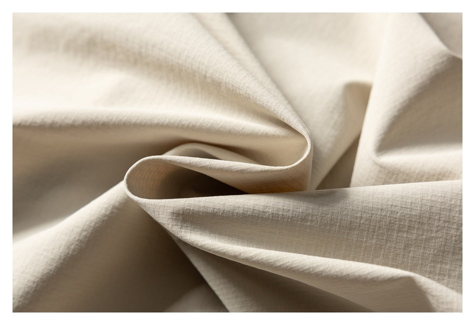 Close-up of light beige fabric draped in soft folds, showing its subtle woven texture.