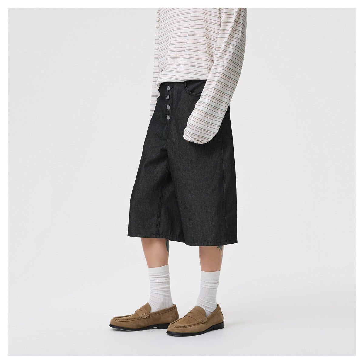 Angled front view of a model wearing black knee-length wide-leg denim shorts with a button fly.