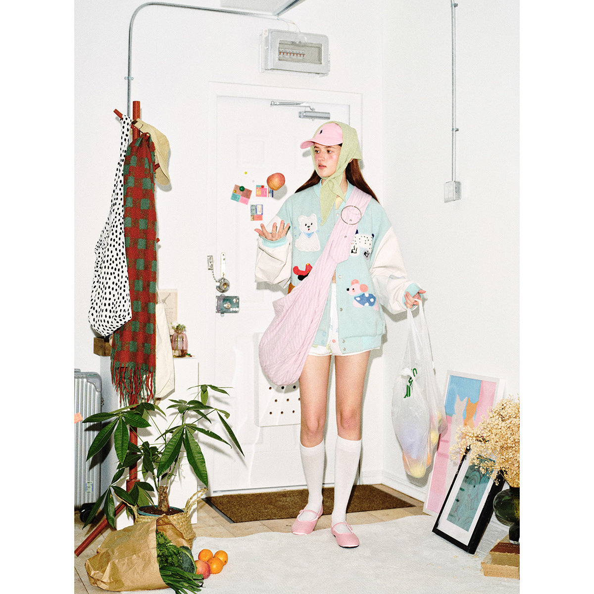 Model wearing a pale aqua varsity jacket with white sleeves and animal patches, paired with shorts and a pink quilted