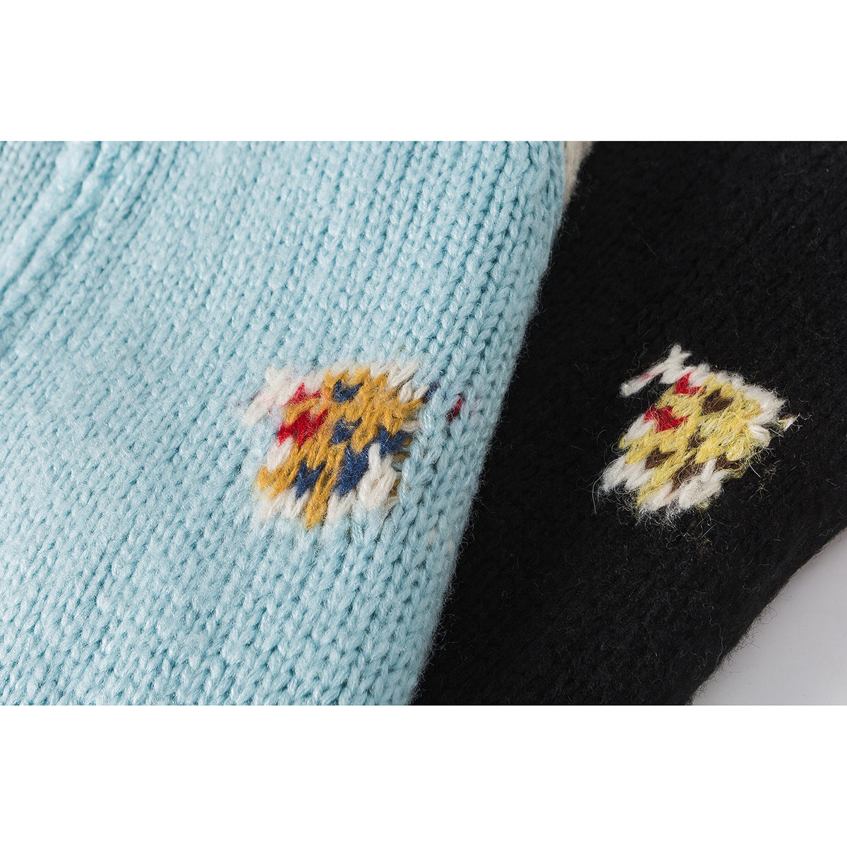 Close-up of colorful embroidered motifs on pale blue and black knit cardigan panels.