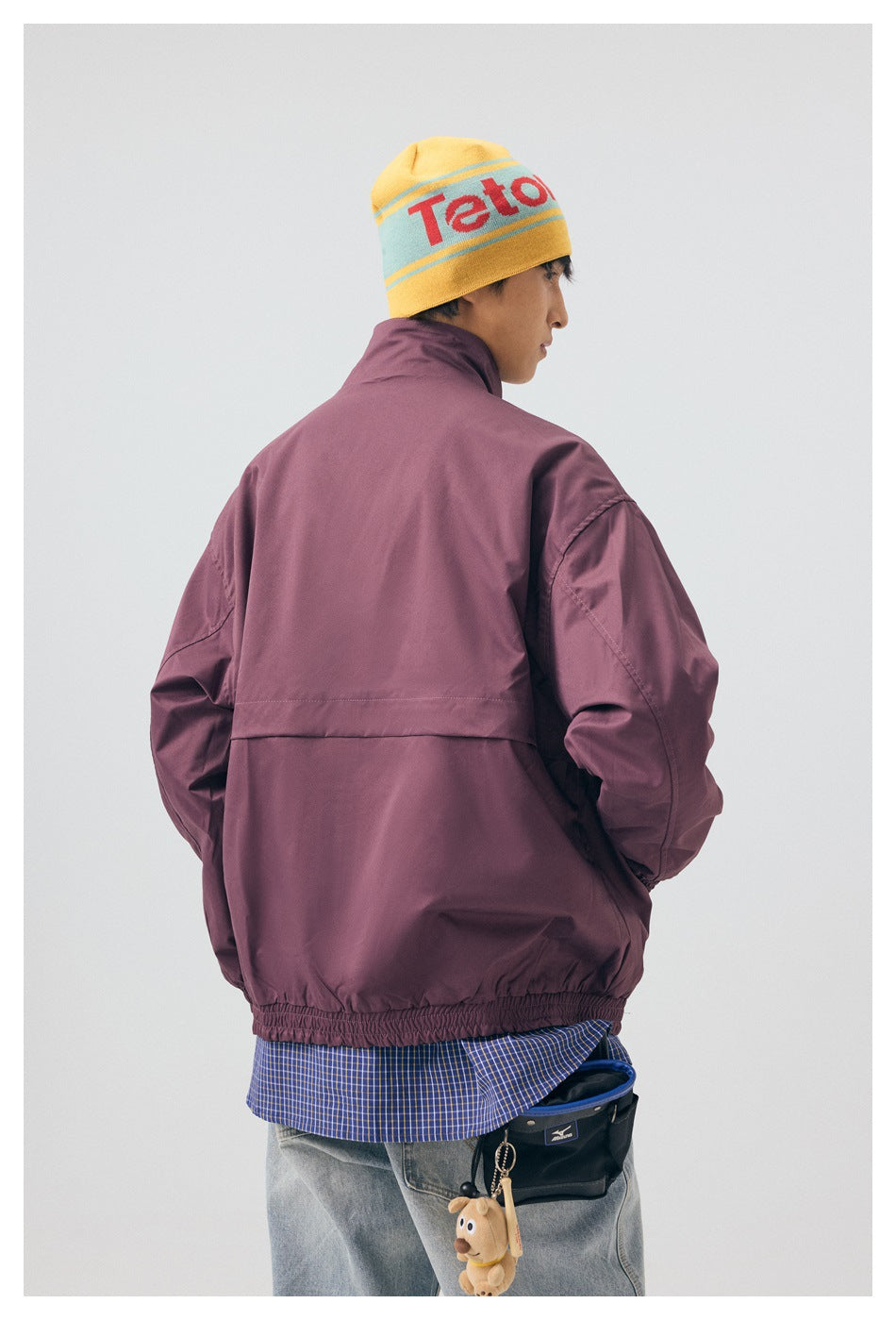 Back view of a model wearing a plum jacket with a horizontal back seam and gathered hem.