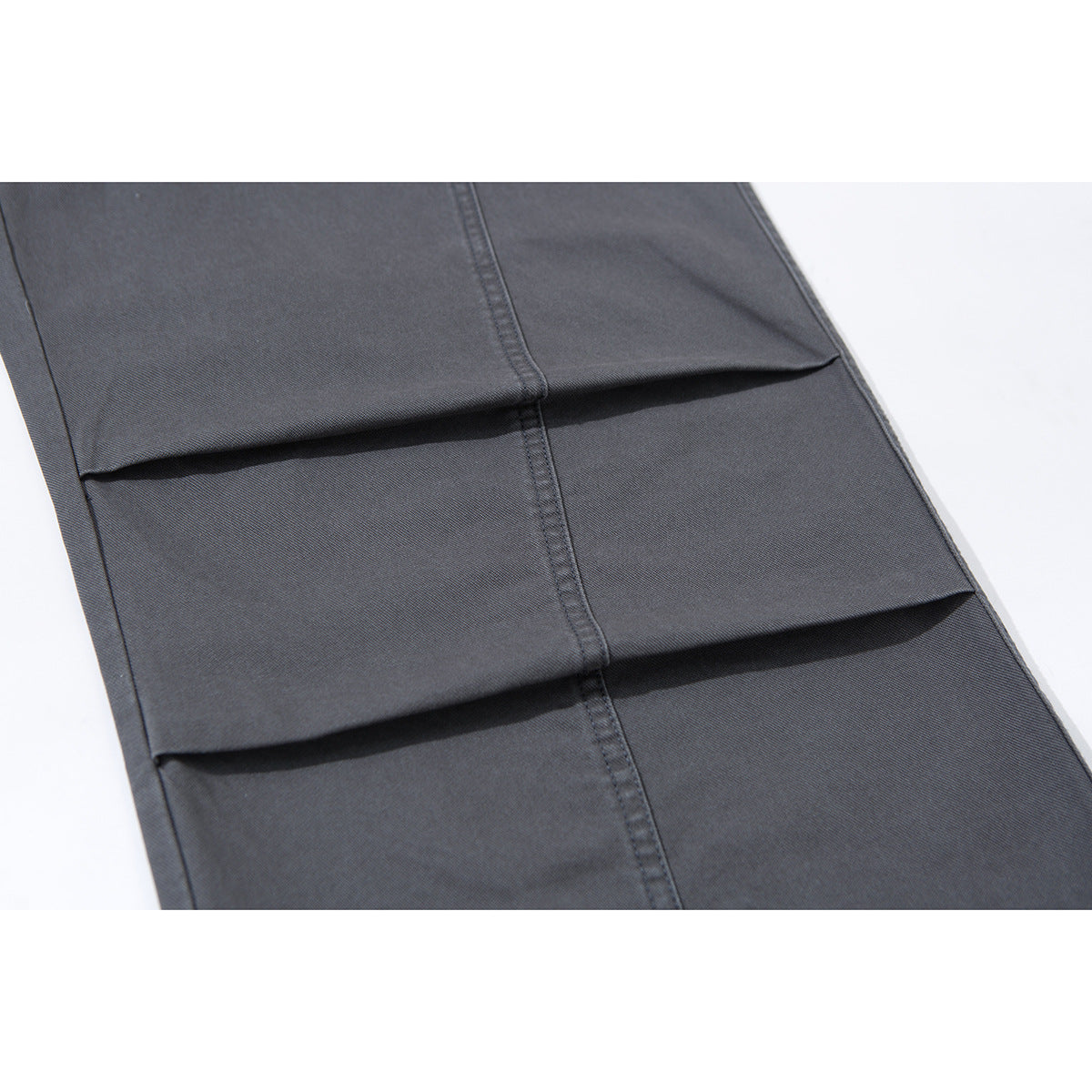Close-up of charcoal-gray trouser legs showing stitched vertical seams and layered horizontal pleats.
