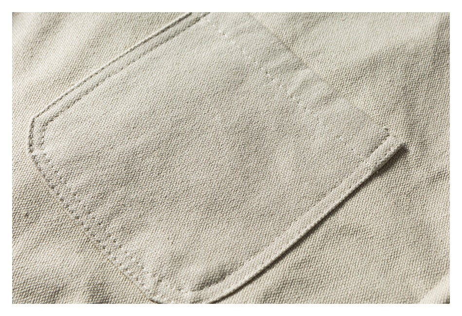 Close-up of a stitched patch pocket on beige fabric.