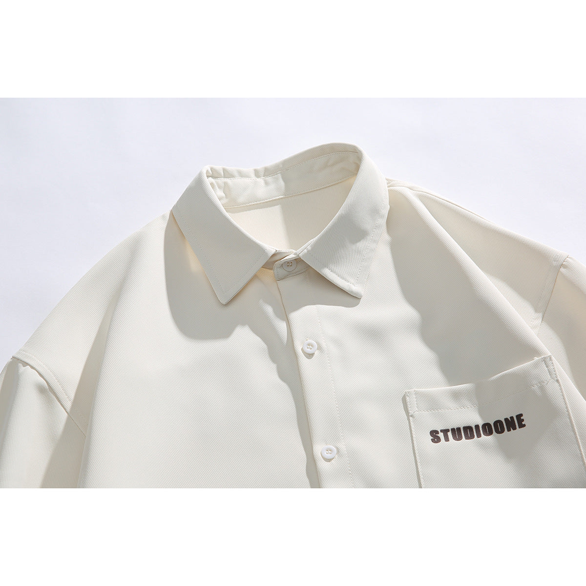Close-up of an ivory short-sleeve button-up shirt showing its pointed collar, buttons, chest pocket, and printed lettering.